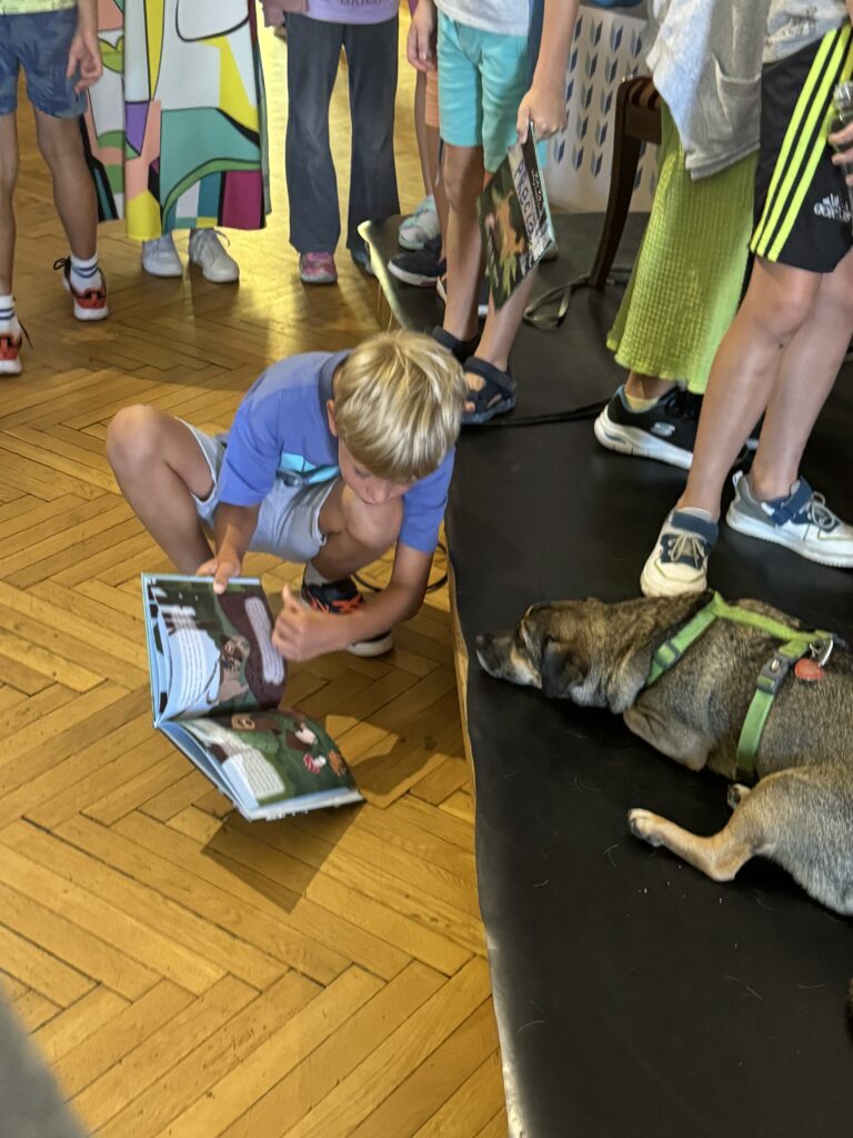 chłopiec czytający książkę "Przygody psa Precla", obok pies Precel, bohater książek